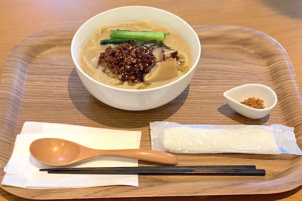 お盆の上に乗った横浜ヴィーガンラーメン。白濁色のスープに小松菜や肉味噌が乗っている。